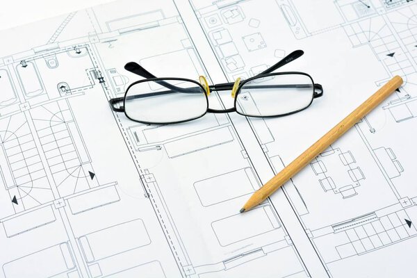 A pencil and glasses on an architectural plan of a house