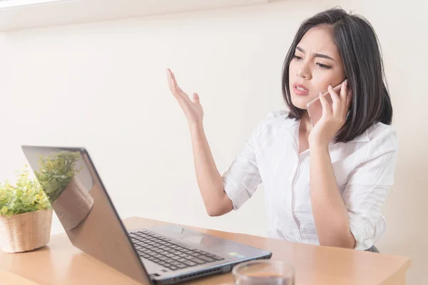 Furious businesswoman wearing suit working on line using a smart phone in a desk at office. Business problem.