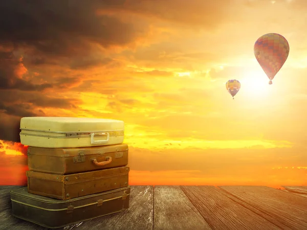 Stacked leather luggage on wood plank with hot air balloons in sunset sky background. Travel concept. Best journey with fantasy nature background.