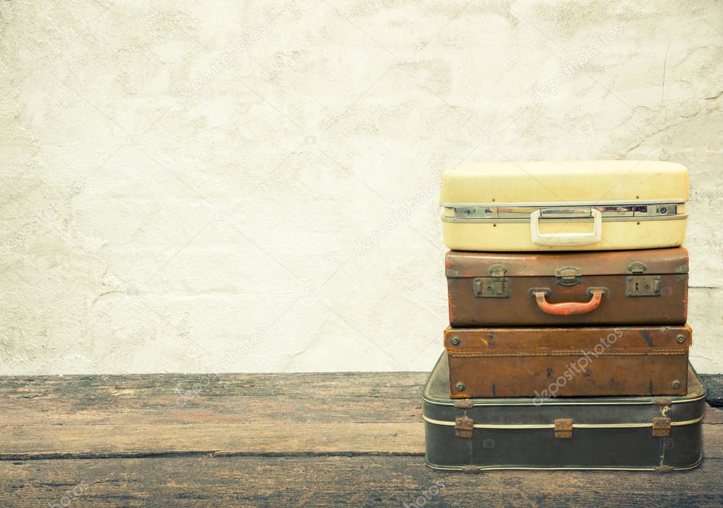 Stacked leather luggage on wood plank with old concrete background. Travel concept.