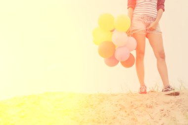 Renkli balonlar kum üzerinde tutan genç kız.