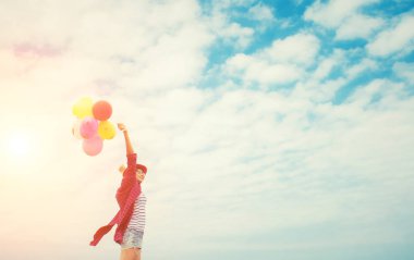 Parlak gökyüzü ve sm renkli balon tutan genç kız