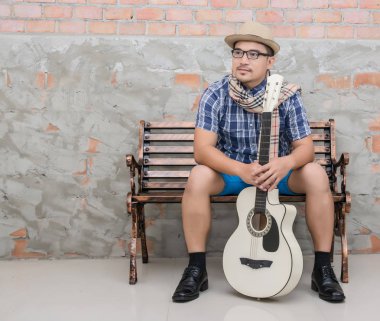 Gitarını içinde ileri geri tutarak bankta oturan genç hipster adam