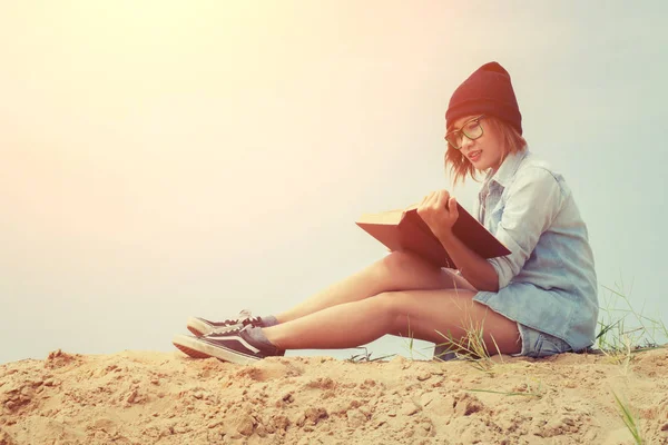 Jovencita leyendo libro y sentada en la playa con el amanecer — Foto de Stock