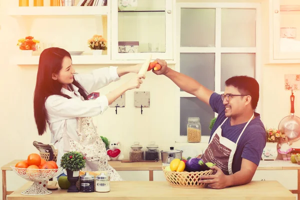 Asian couple in kitchen teasing each other with the vegetables w — Stock Photo, Image