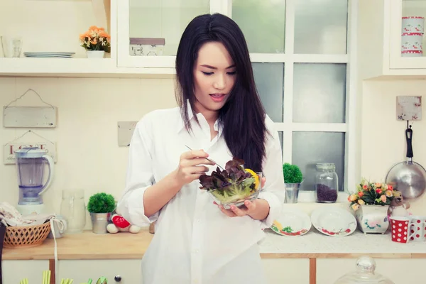 Beautiful young asian woman having green salad in kitchen — Stock Photo, Image