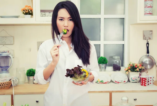 Beautiful young woman eating a healthy salad in the kitchen — Stock Photo, Image