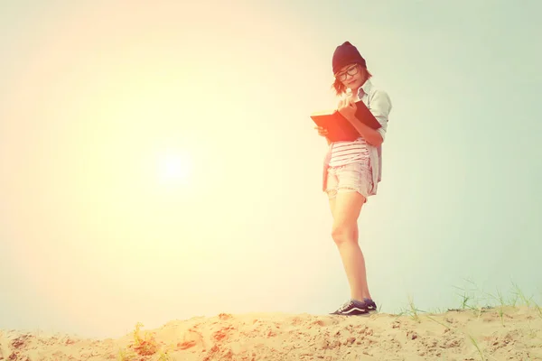 Beautiful young woman reading book standing on the sand look so — Stock Photo, Image