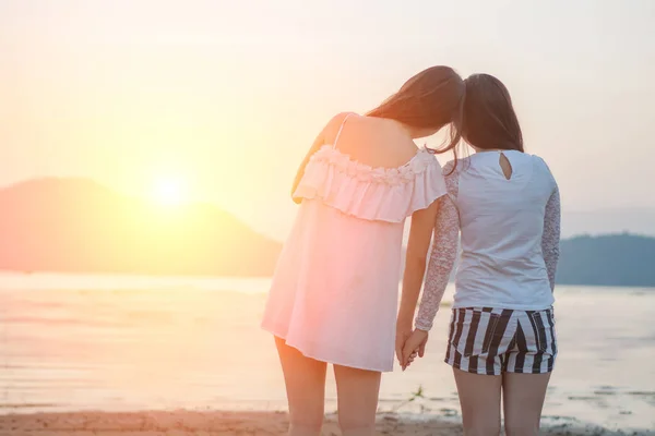 Due giovani donne si tengono per mano insieme sulla spiaggia guardando i soli — Foto Stock