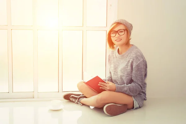 Hermosa joven sentada leyendo libro cerca de la ventana mira a c — Foto de Stock