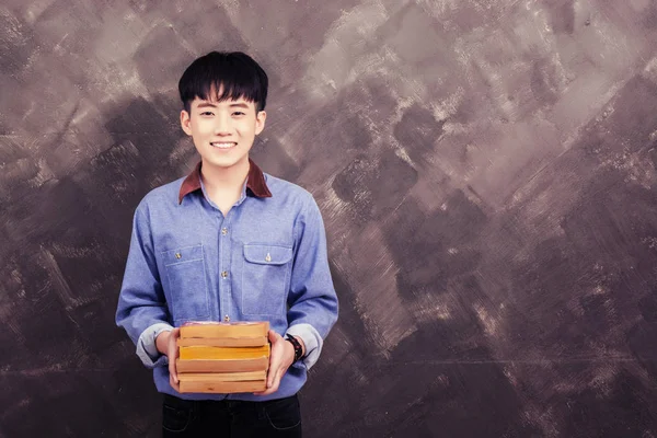 Schöner junger asiatischer Mann mit Buch auf dem Grunge Wall Smiley — Stockfoto