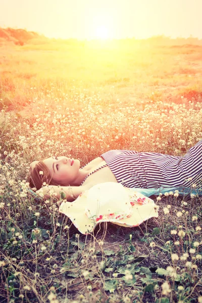 Молодая сексуальная женщина, лежащая в траве в шапке, смотрит в небо — стоковое фото