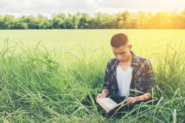 Doğa ile kitap okuma otlakta oturan genç hipster adam 