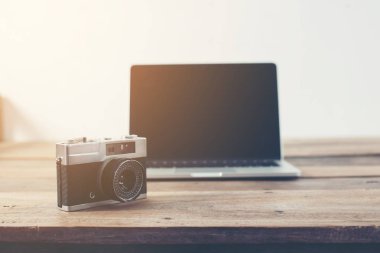 dizüstü bilgisayar ve retro fotoğraf makinesi retro ses tonuyla ahşap masa üstünde.