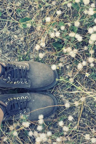 Les pieds des femmes avec des bottes de femmes brunes dans le champ de fleurs . — Photo