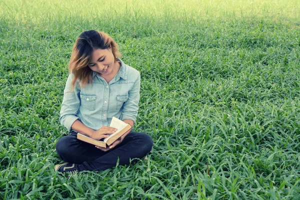 Ung kvinna läsa en bok i parken på gräset. — Stockfoto