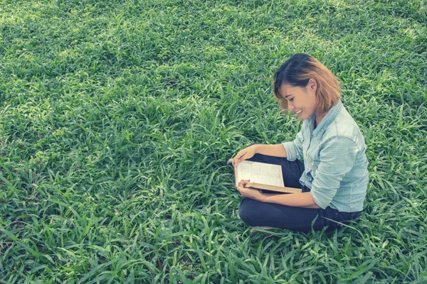 Genç kadın parkta çim bakmak çok mutlu bir kitap okuma.