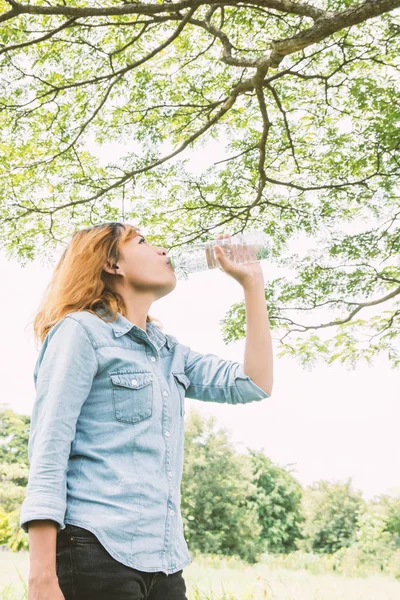 Mooie jongedame drinkwater in zomer groen park. — Stockfoto