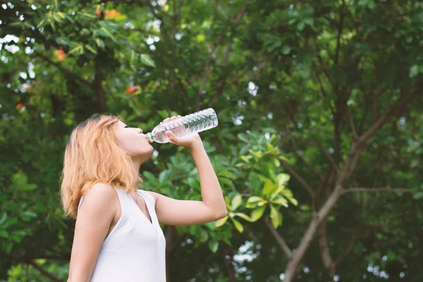 Mooie jongedame drinkwater op groen park. — Stockfoto