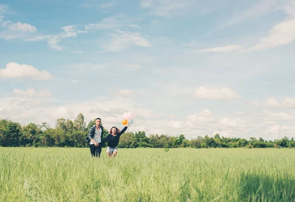 Young Couple running and holding balloon in the green grass belo — Stock Photo, Image