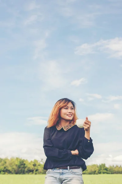 Jeune femme hipster debout sur la prairie tenant du café chaud et — Photo
