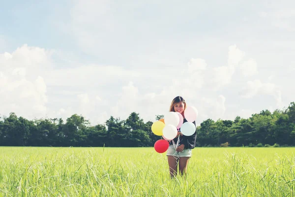 Gelukkig mooie jongedame en kleurrijke ballonnen in grasland. — Stockfoto