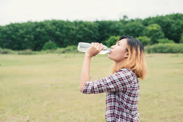 Jonge hipster vrouw drinkwater in zomer groen park. — Stockfoto