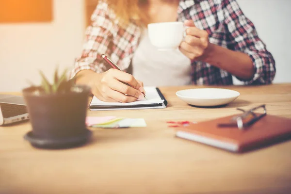 Mujer de negocios sosteniendo una taza de café y escribir un plan de negocios —  Fotos de Stock