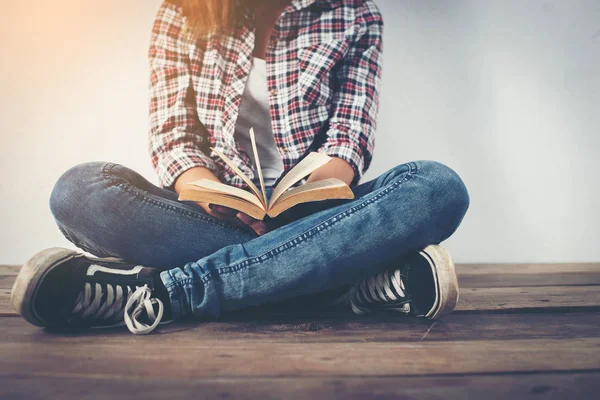 Молода хіпстерка тримає відкриту книгу, сидячи на дерев'яній підлозі . — стокове фото