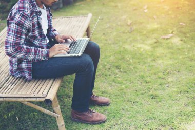 Güneşli bir gün, bilgisayarda parkta genç hipster adam eser.