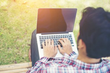 Güneşli bir gün, bilgisayarda parkta genç hipster adam eser.