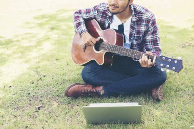 Genç hipster adam uygulanan gitar ile laptop parkta, mutlu