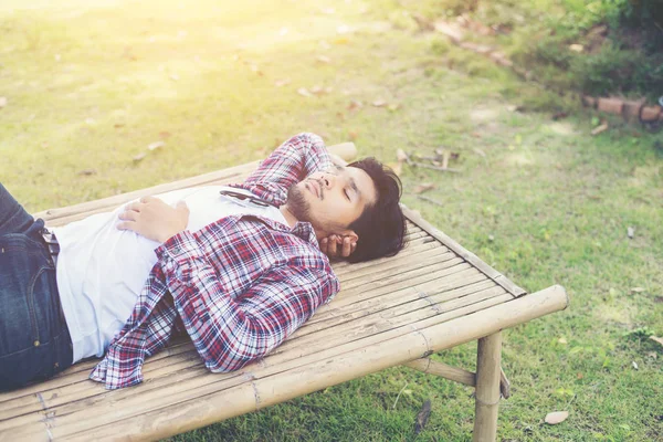 Glücklicher junger Hipster liegt auf Bank im Naturpark. — Stockfoto