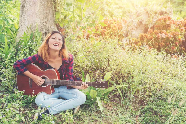 Young beautiful hipster woman playing guitar sitting on grass in — Stock Photo, Image