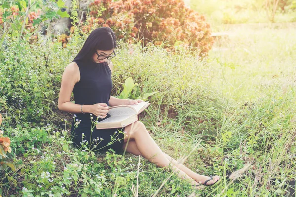Relajada joven hermosa mujer leyendo un libro en el césped con su — Foto de Stock