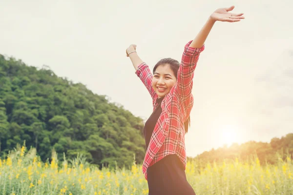 Jovem mulher feliz levantando as mãos no campo de flores amarelas no pôr do sol — Fotografia de Stock