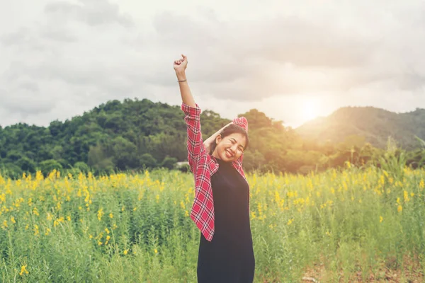 Young happy woman raising hands in yellow flower field on sunset