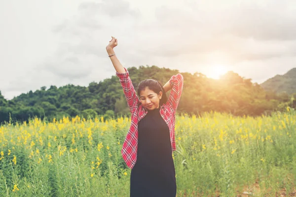 Jovem mulher feliz levantando as mãos no campo de flores amarelas no pôr do sol — Fotografia de Stock