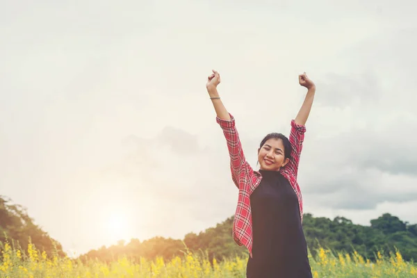 Jovem mulher feliz levantando as mãos no campo de flores amarelas no pôr do sol — Fotografia de Stock