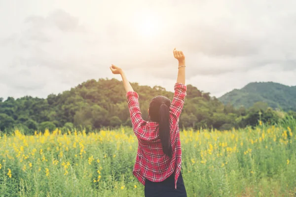 Jovem mulher feliz levantando as mãos no campo de flores amarelas no pôr do sol — Fotografia de Stock