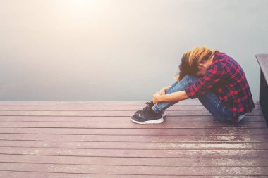 İskelede üzüntü ile oturan üzgün hipster kadın.