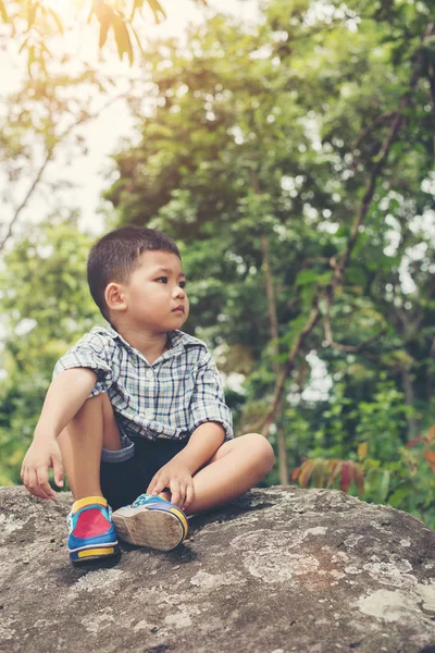 Sad little boy sitting on rock, in park. — Stock Photo, Image