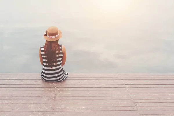Back of young woman wearing hat sitting at the pier,relaxing enj — Stock Photo, Image