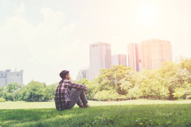Parkta yalnız karşı çimenlerin üzerinde oturan genç hipster adam
