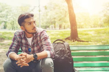 Genç hipster adam ahşap bir bankta oturan yanında sırt çantası ile