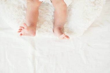 Yeni doğan bebek bacakları beyaz yatakta.