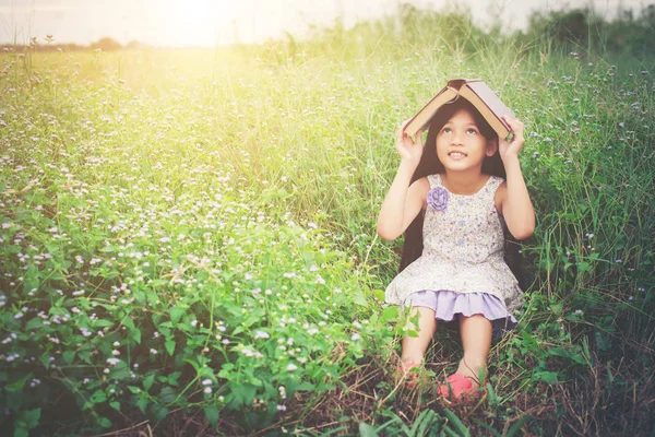 Little cute asian girl cover book on her head at nature. — Stock Photo, Image