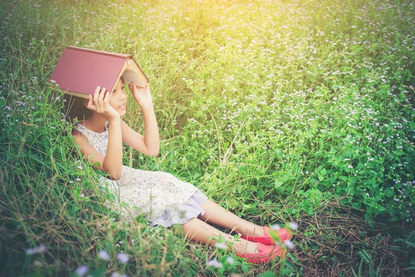 Piccolo carino asiatico ragazza copertina libro su il suo testa a natura . — Foto Stock