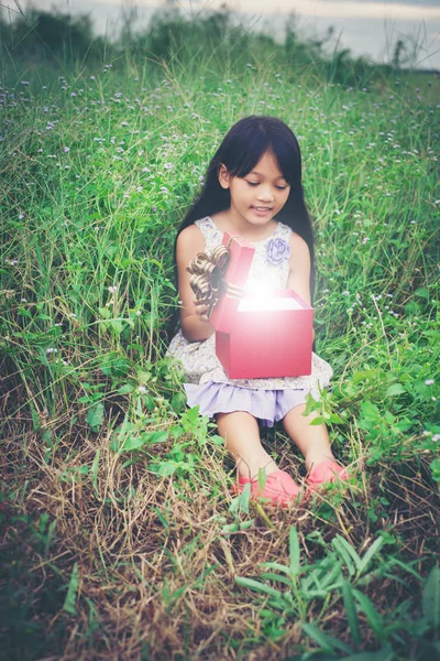 Menina sentada no campo com um presente e olhando para ele , — Fotografia de Stock