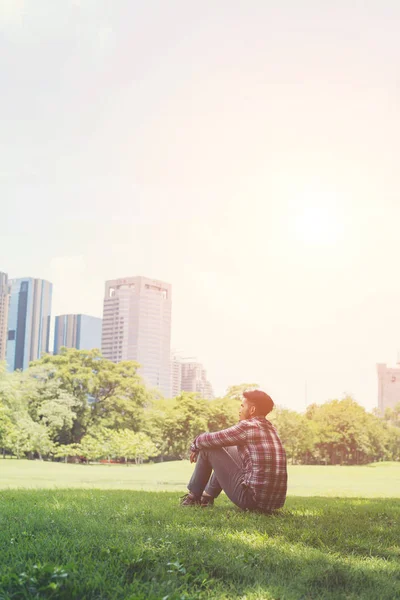 Jonge hipster man zit op gras in het park alleen tegen de — Stockfoto